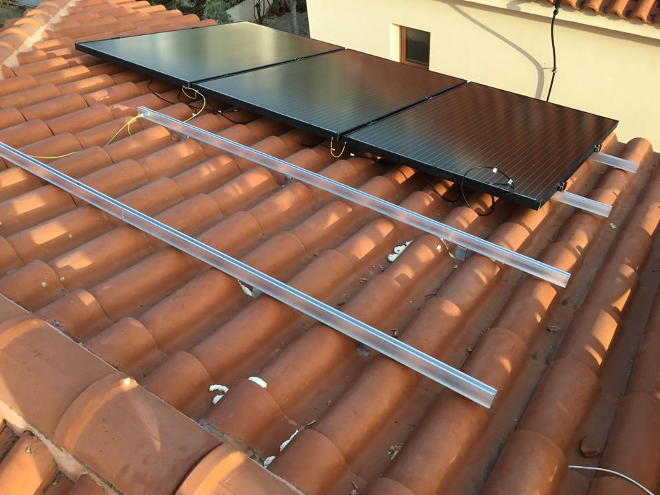 Black solar panels being fitted to mounting rails on a tiled roof in Frenaros